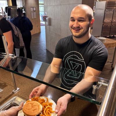 Student being handed a plated burger and fries from the grill station at Fresh Food Co